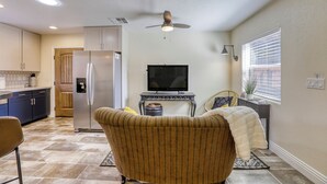 Un espacio habitable compacto con kitchenette, televisión, ventilador de techo y ventana con persianas.