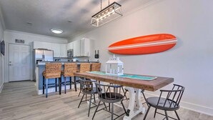 Un comedor con una mesa de madera, sillas de mimbre y una decoración con una tabla de surf en la pared.