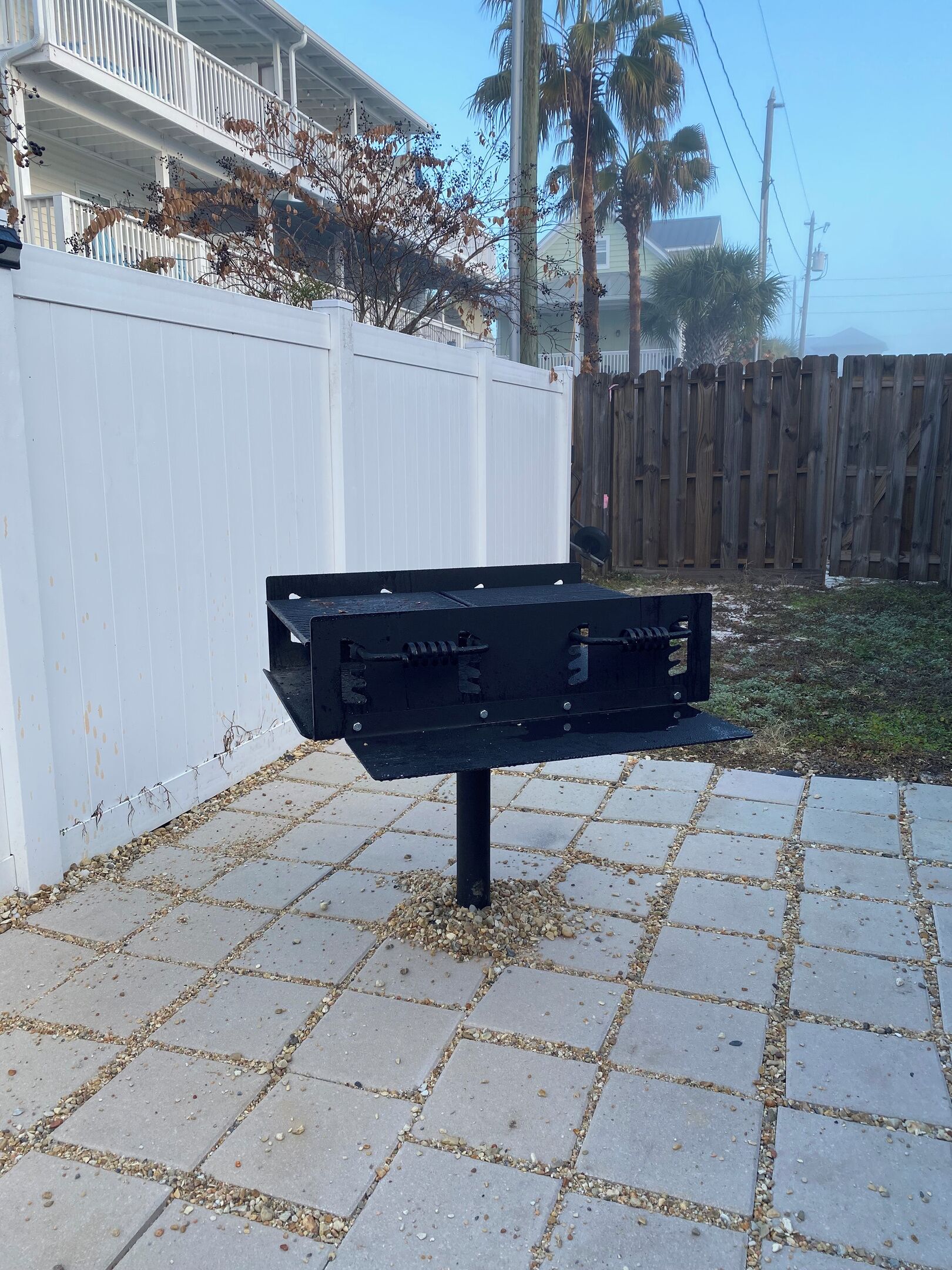 A black metal object on a paved surface with a white fence and a wooden fence in the background.