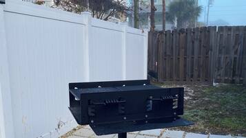 A black metal object on a paved surface with a white fence and a wooden fence in the background.