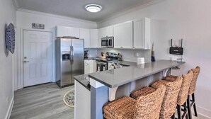 Una cocina moderna con armarios blancos, un refrigerador de acero inoxidable, un microondas e isla incorporada con taburetes de bar.