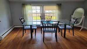 A dining area with a glass table and chairs, large windows, and a white curved mirror.