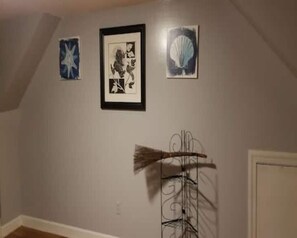 Ein Zimmer mit schrägem Dach, einem an einer Wandhalterung hängenden Besen und drei gerahmten Kunstwerken.