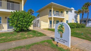 A multi-story hotel with balconies, a palm tree sign, and a well-maintained lawn. - Private 2 bedroom 1 bath with pool, beach, wifi, near Daytona & I-4 to Orlando (Ormond Beach)