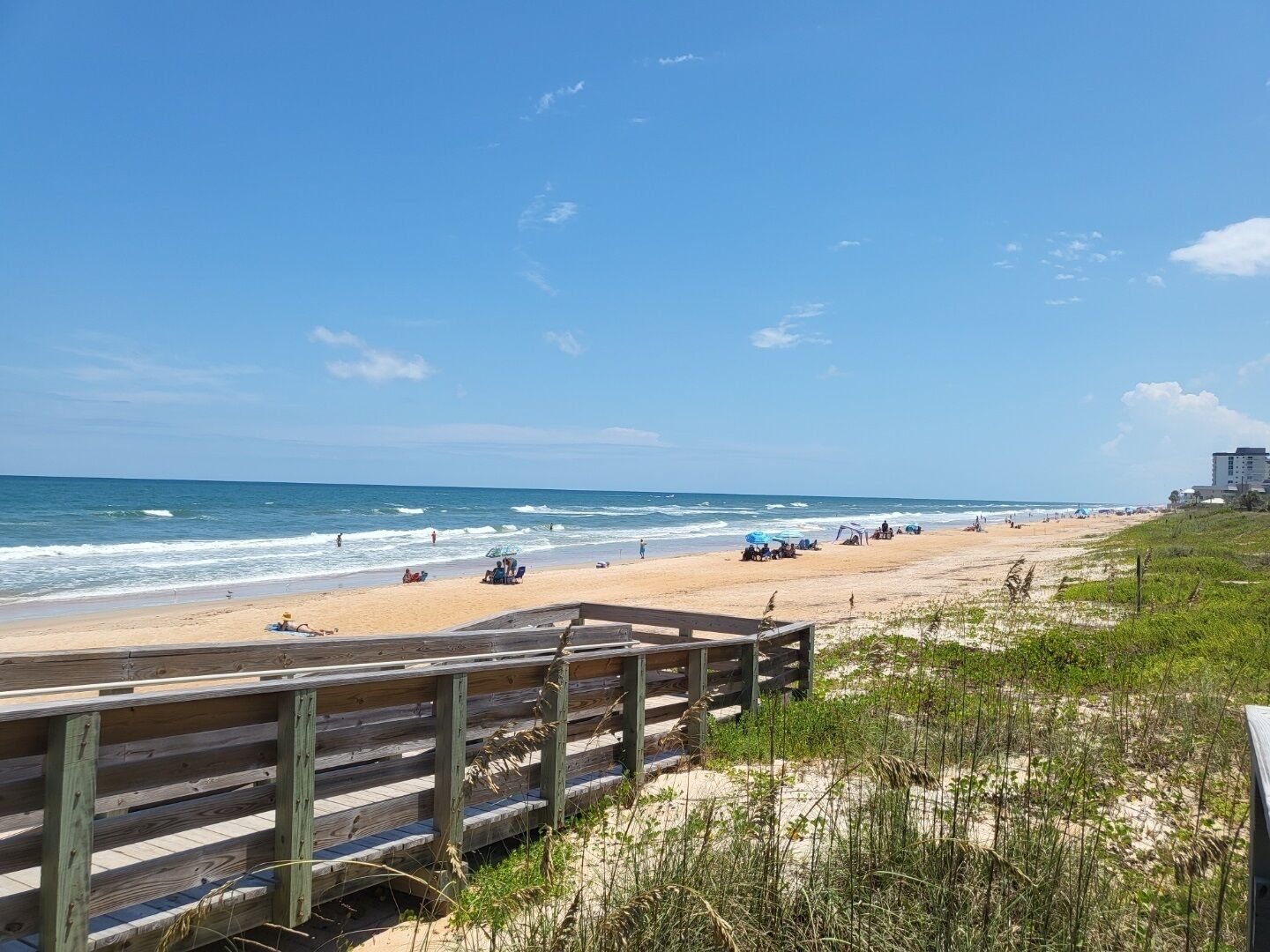 Una playa con un paseo marítimo de madera, arena y olas del océano.