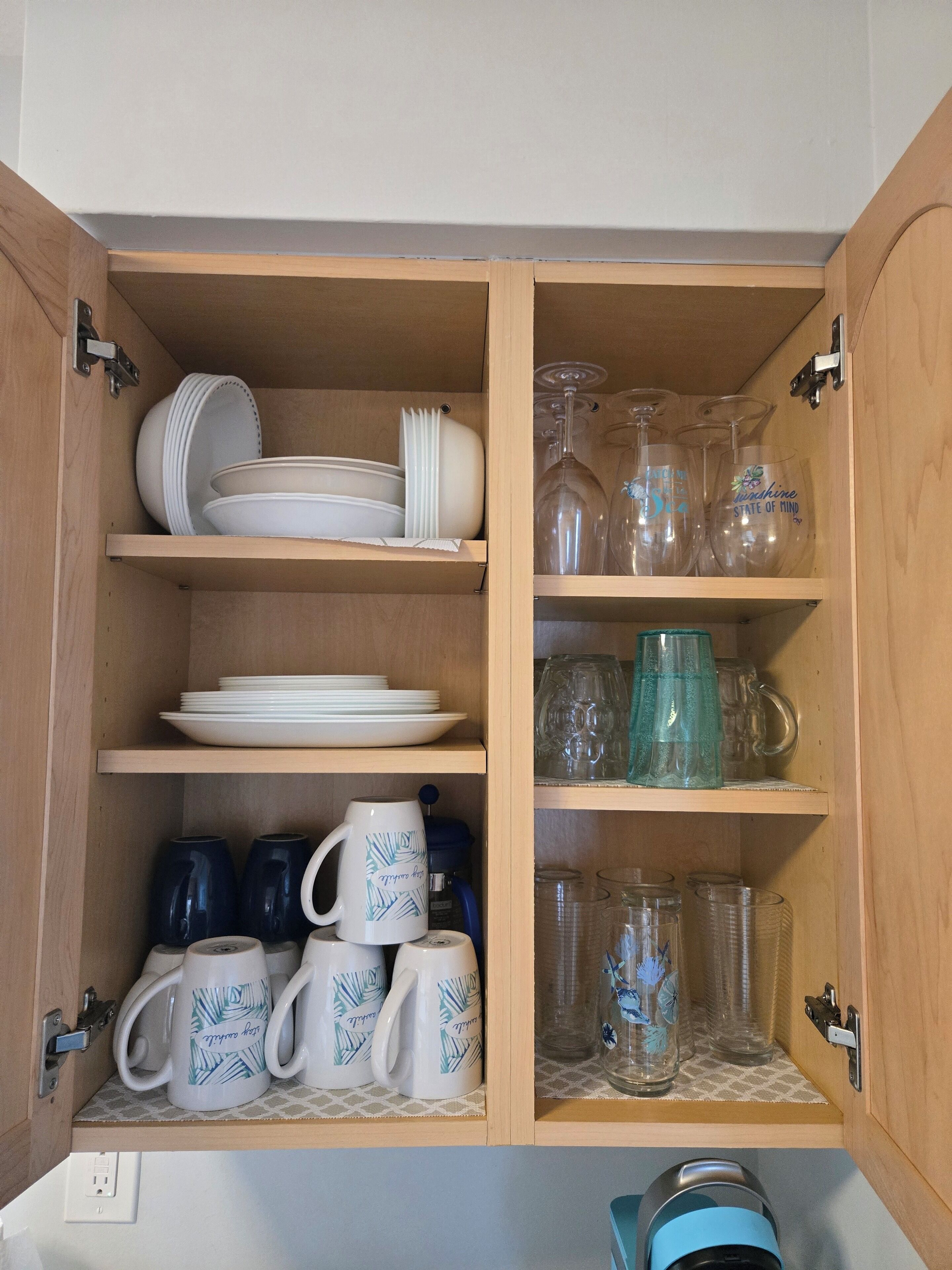A wooden cabinet with shelves containing white plates, bowls, and cups with leaf patterns.