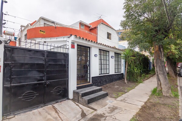 A two-story house with a black gate, a small porch, and a pathway leading to the entrance.