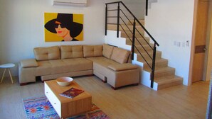 A modern living room with a sectional sofa, a wooden coffee table, a colorful rug, a staircase with a black railing, and a painting on the wall. - Zehn House in Girardot (Ricaurte)