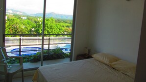 A bedroom with a bed, a chair, and a view of a swimming pool and greenery. - Zehn House in Girardot (Ricaurte)