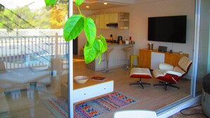 A modern kitchen with a bar area, a dining space with a red and white chair, and a television mounted on the wall. - Zehn House in Girardot (Ricaurte)