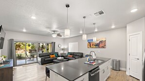 A modern kitchen with a central island, a dining area with a black leather couch, and a view of a garden through large sliding doors. - Bike, Hike, Swim, Explore 5 Star Resort - Guaranteed FUN & Memories (St. George)