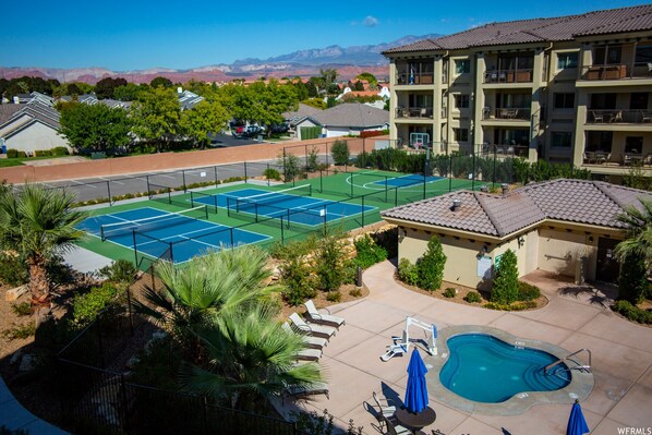 A tennis court, a swimming pool, and a building with balconies.