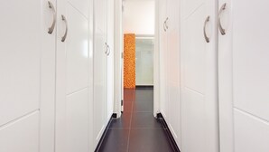 A corridor with white lockers and a tiled floor leading to a bathroom with an orange and yellow patterned wall.