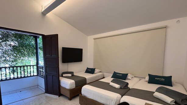 A hotel room with three beds, a TV, and a balcony.