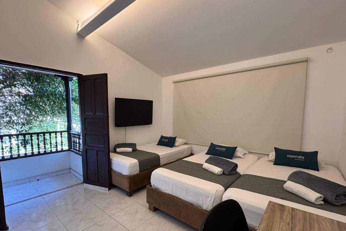 A hotel room with three beds, a TV, and a balcony.