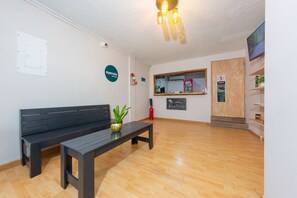 Un área de recepción con un banco de madera, una pequeña mesa con una planta, un extintor y un letrero que indica una zona para fumadores.