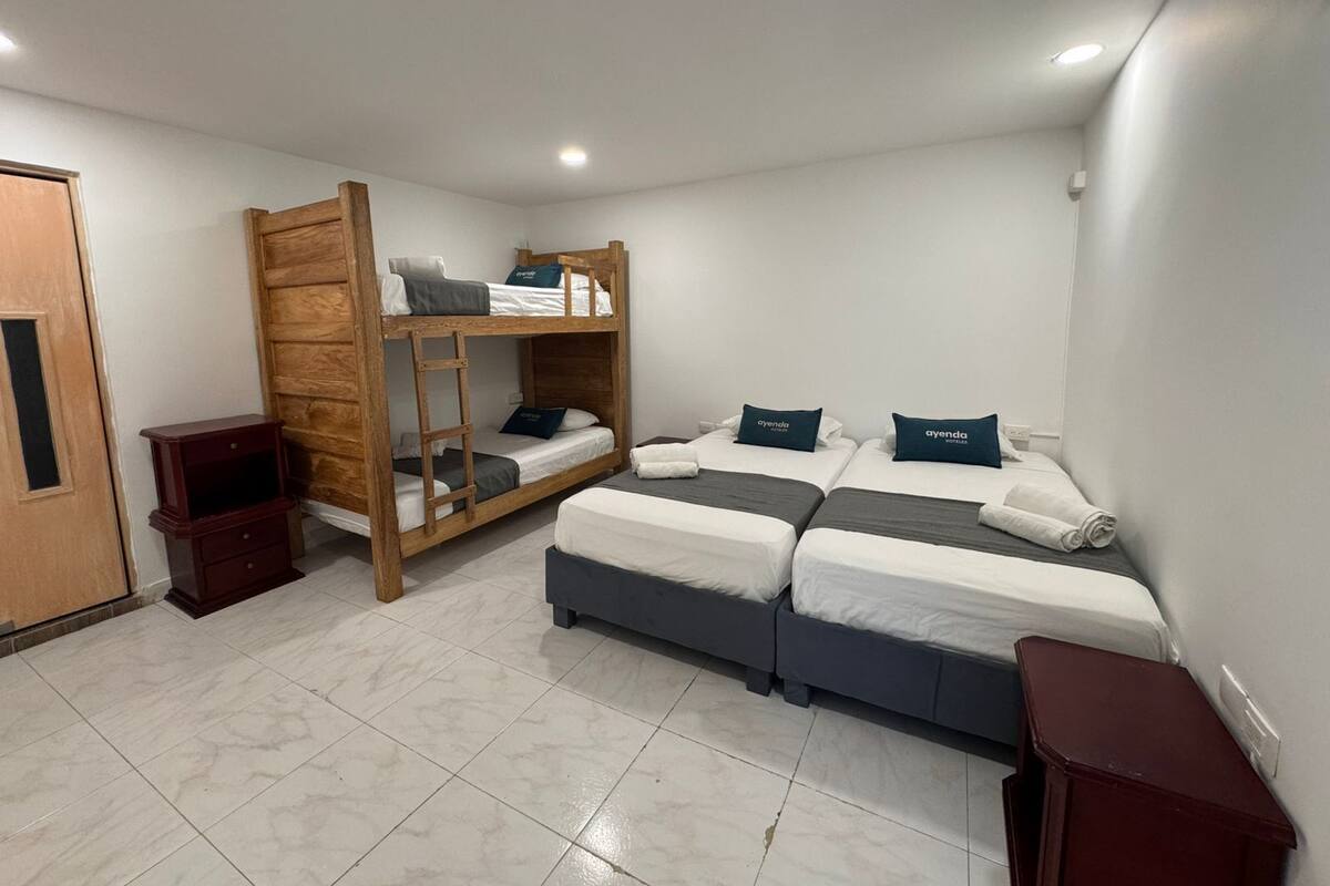 A room with bunk beds, two single beds, a small wooden cabinet, and a door.