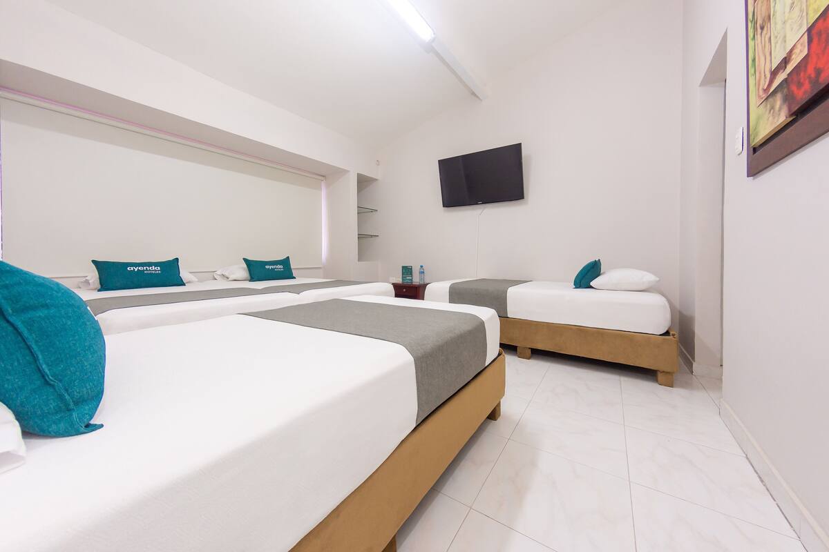A hotel room with three beds, a flat-screen TV mounted on the wall, and a tiled floor.
