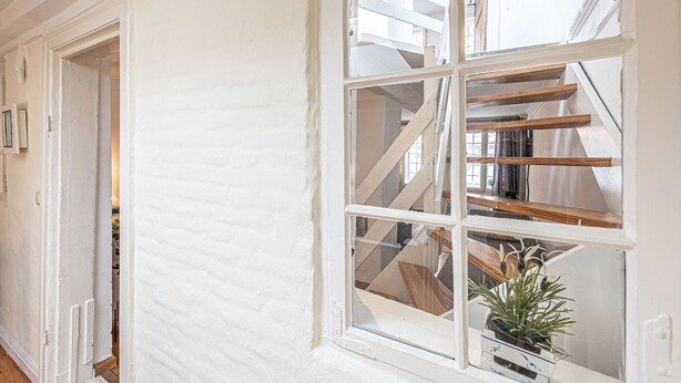 Un pasillo de paredes blancas con un ventanal que da a una escalera de madera.