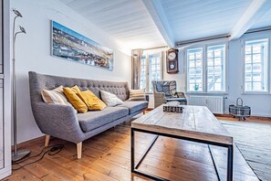 A living room with a grey sofa, a wooden coffee table, and a large window with a view of a cityscape.