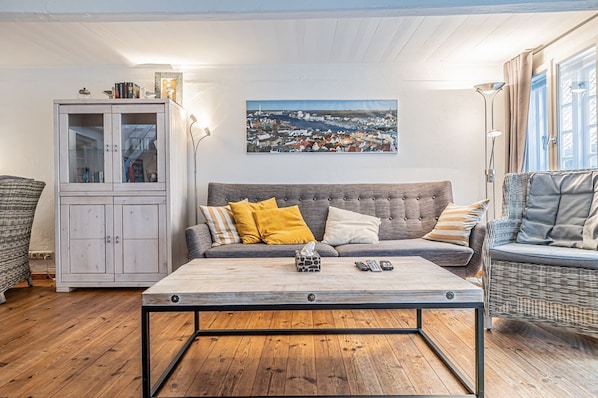A living room with a grey sofa, a wooden coffee table, a wicker armchair, and a cabinet with glass doors.