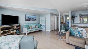 Ein geräumiges Wohnzimmer mit einem großen Flachbildfernseher, einem hellblauen Sofa, einem beigefarbenen Sofa und einer Holz-Unterhaltungseinheit.
