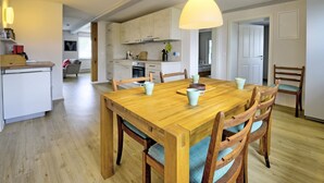 A modern kitchen with white cabinets, a wooden dining table with chairs, and a hanging pendant light.