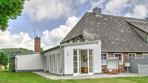 A two-story house with a sloped roof, a brick chimney, and a white exterior.
