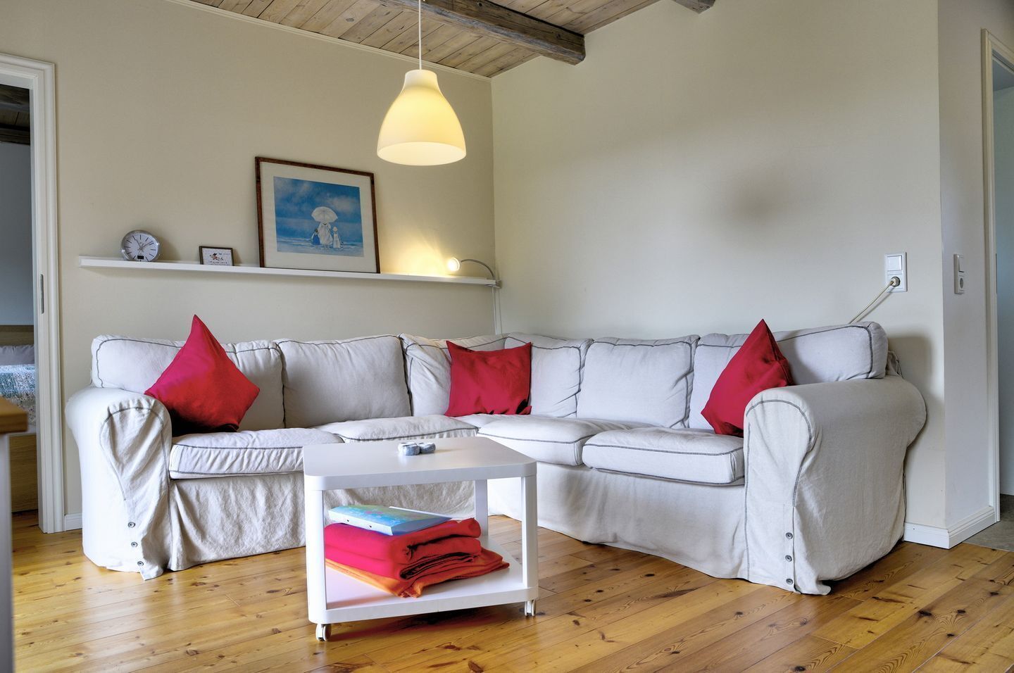 A modern living room with a white sectional sofa, red cushions, a small white side table, and a pendant light.