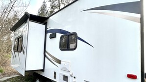 Un camper bianco con una portella laterale, un piccolo oblò e uno specchietto retrovisore.