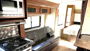 Cucina compatta per camper con fornello, microonde e una piccola zona pranzo con tavolo e panca.