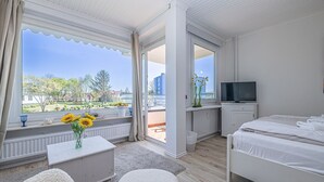 Habitación de hotel moderna con un ventanal grande, un televisor de pantalla plana, una cama, una mesita con un jarrón de flores y vistas al exterior.