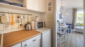 Una cocina moderna con armarios blancos, encimera de madera y lavavajillas Siemens. Hay una zona de comedor con una mesa y sillas, y vistas al exterior a través de una ventana.