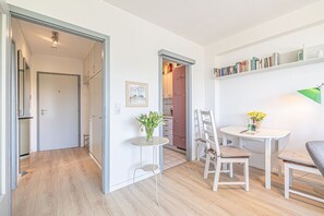 Un intérieur moderne avec un plancher en bois, un coin repas comprenant des chaises et une table, une bibliothèque et une porte donnant sur une autre pièce.
