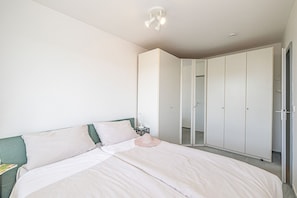 Un dormitorio con cama, mesita de noche, armario y lámpara de techo.