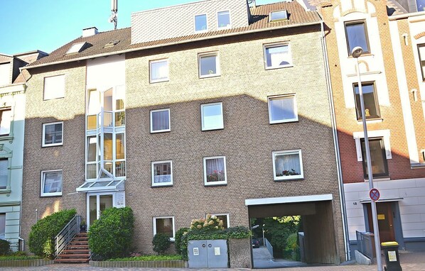 A multi-story residential building with a brick facade, multiple windows, a staircase, and a small garden area.
