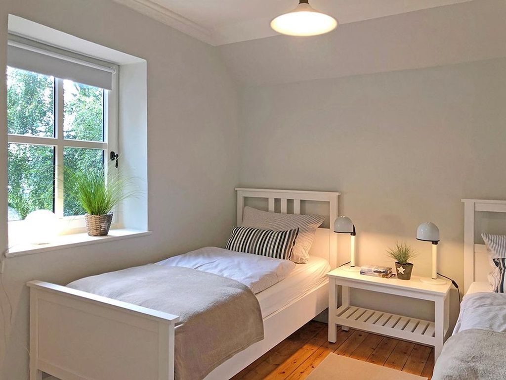 A bedroom with a single bed, bedside tables, a window with a view of greenery, and a ceiling light.