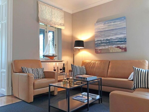 Un salon avec deux canapés beige, une table basse en verre et un tableau représentant la mer accroché au mur.