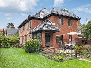 Une maison à deux étages, construite en briques, dotée d’un patio couvert et d’une pelouse.
