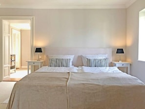 A bedroom with a large bed, two bedside tables with lamps, and a door leading to a hallway.