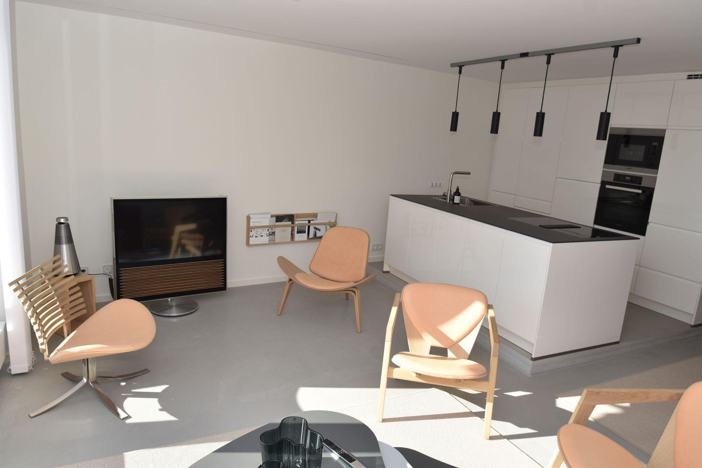 Una sala de estar moderna con televisor, asientos y una zona de cocina.