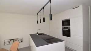 Una cocina moderna con isla central, horno empotrado e iluminación colgante.