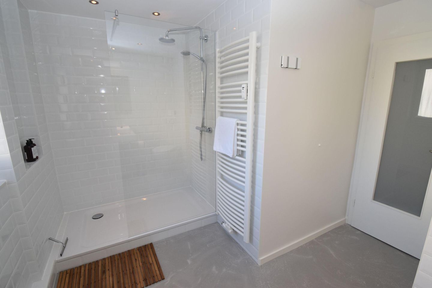 A modern bathroom with a glass shower enclosure, a white towel rack, and a wooden mat.