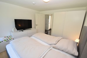 A bedroom with a bed, a TV, a clock, and a wardrobe. - fewo1846 - Solskin - fewo1846 - Solskin / comfortable 3-room apartment in a rural location (Flensburg)