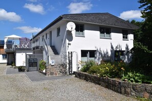 A two-story building with a satellite dish, a gated entrance, and a small garden. - fewo1846 - Solskin - fewo1846 - Solskin / comfortable 3-room apartment in a rural location (Flensburg)