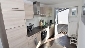Una cocina moderna con armarios de madera clara, electrodomésticos de acero inoxidable y una puerta corrediza de vidrio que da a un espacio exterior.