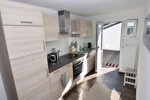 A modern kitchen with light wood cabinets, stainless steel appliances, and a sliding glass door leading to an outdoor area. - fewo1846 - Solskin - fewo1846 - Solskin / comfortable 3-room apartment in a rural location (Flensburg)