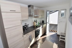 Una cucina moderna con mobili in legno chiaro, elettrodomestici in acciaio inossidabile e una porta scorrevole in vetro che dà su un'area esterna.