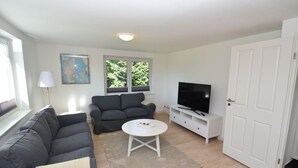 Una sala de estar con un sofá, un televisor sobre un mueble bajo, una lámpara y una ventana.