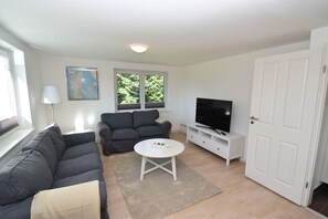 A living room with a sofa, a TV on a stand, a lamp, and a window.